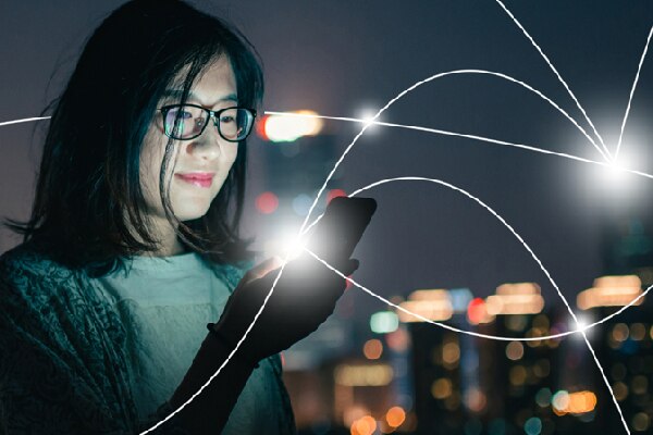 A woman looking at her phone with a nighttime city in the background and graphics depicting a IOT network