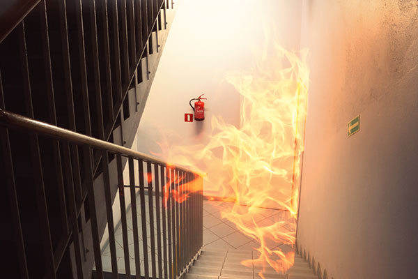 Looking down a staircase at an apartment on fire with an extinguisher in the background
