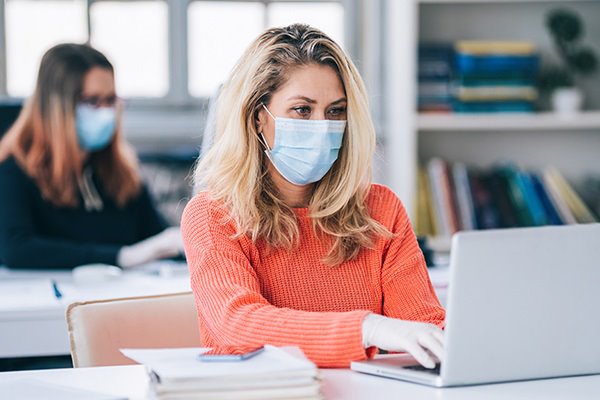 Woman wearing a surgical face mask working on her laptop