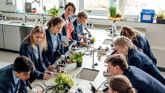 Students with their teacher in a laboratory with microscopes on the table