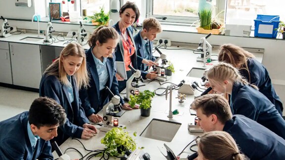 Students with their teacher in a laboratory with microscopes on the table