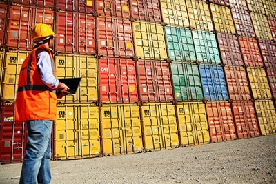 Person in a safety gear looking at containers at a shipping container yard