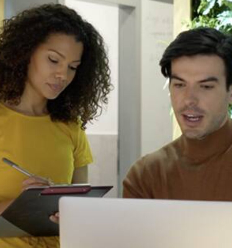 A man working on a laptop and a women writing on notepad