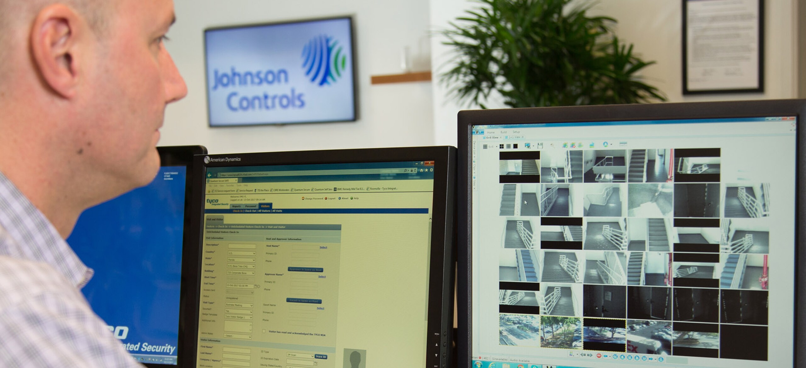 A man looking at a computer screen with CCTV footage with a Johnson Controls logo in the background