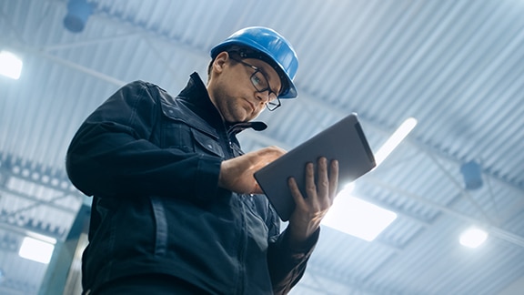 Frog's-eye view of an engineer wearing glasses and protective gear, scorlling on a tablet