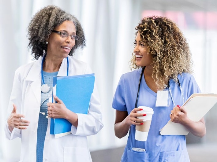 Two female healthcare workers walking down a hospital corridor while chatting