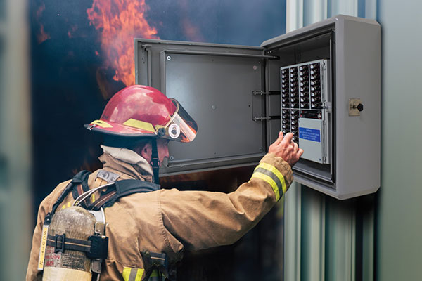 A fire-fighter handling an electric box with a fire in the background