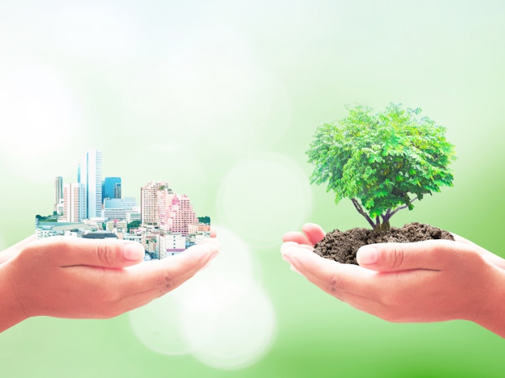 Two pairs of hands holding up a city and a tree to depict ecological balance